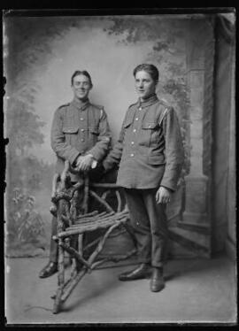 [Two soldiers standing next to a three-legged rustic chair]